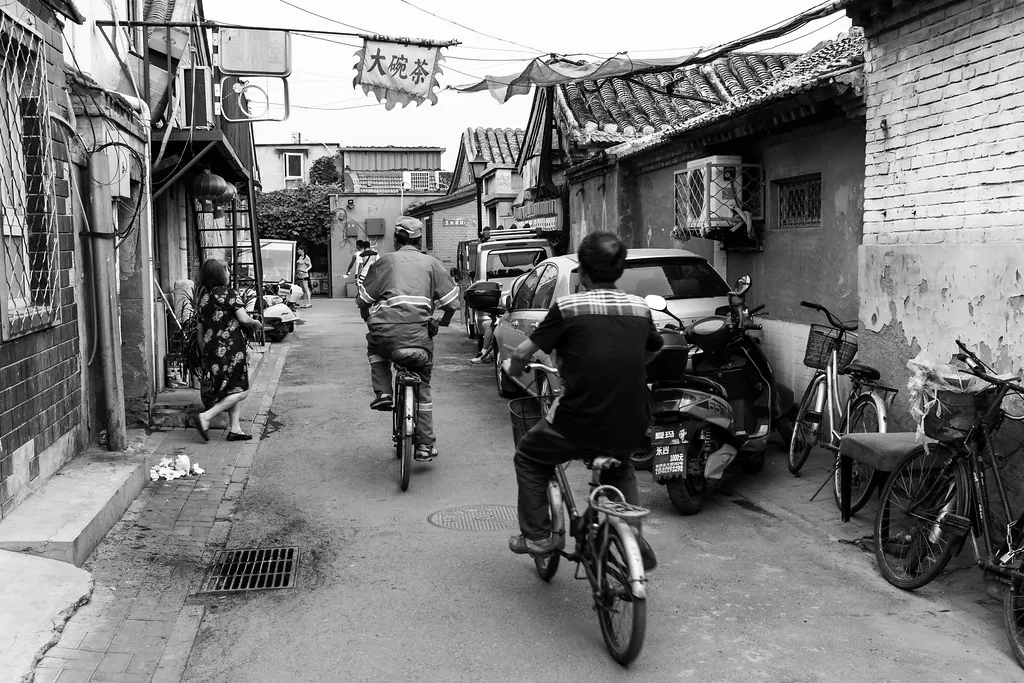 A busy Chinese street at pavement level, shopfronts and passers-by going about an ordinary day.