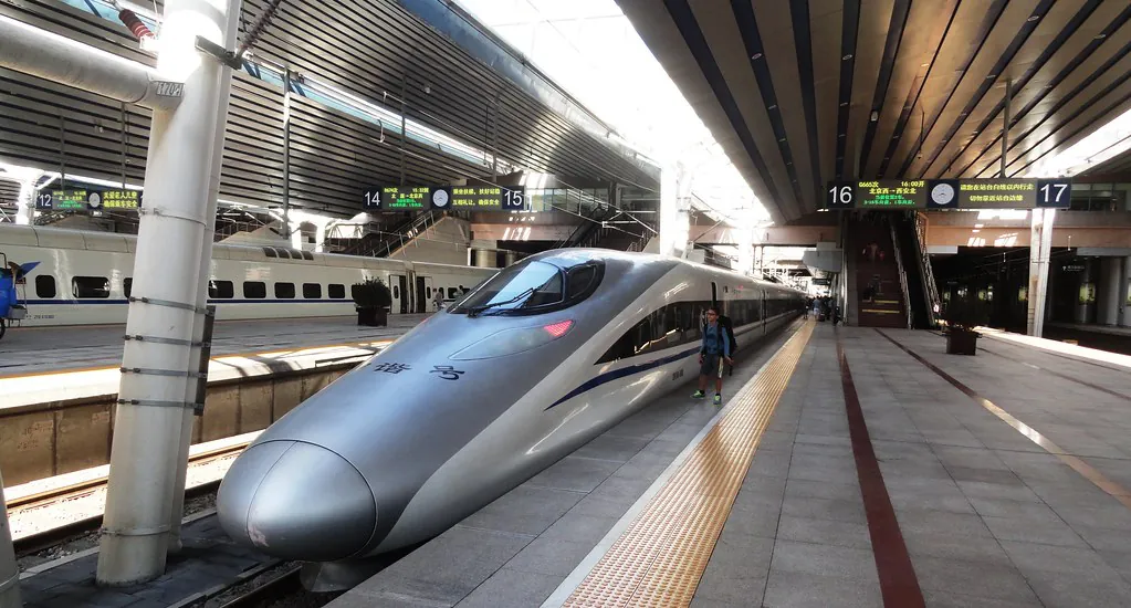 A high-speed train waiting at a Chinese station platform beneath the overhead departure signage.