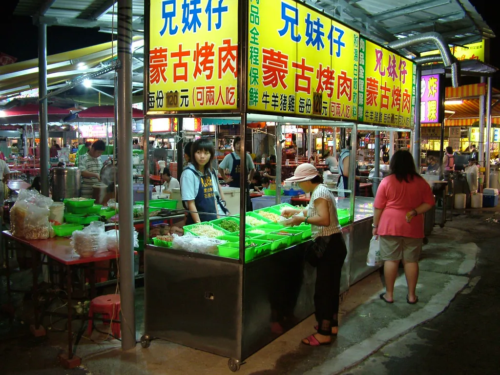 A covered night market in China, every stall sign a large board set in Chinese characters, shoppers walking between the counters.