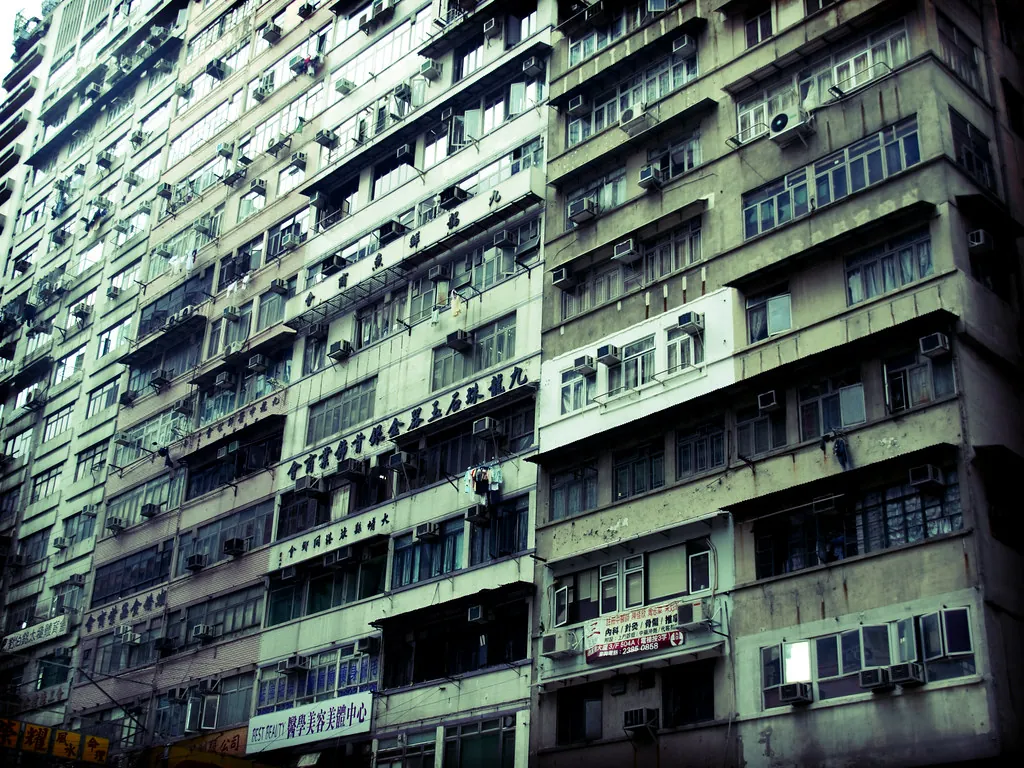 The dense balcony facade of an older Hong Kong tower block, hundreds of flats with window grilles and drying racks.